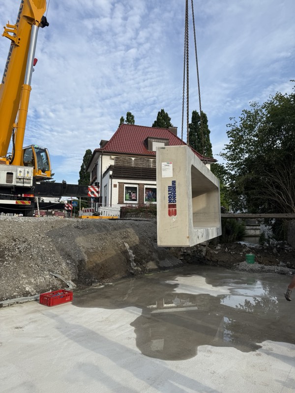 Kran hebt ein Betonfertigteil des Rahmendurchlasses in die Baugrube